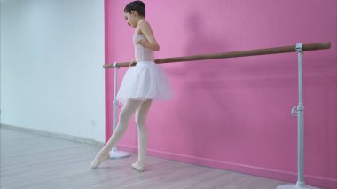 Bir kız bale öğrencisi pembe ve beyaz bir geçmişle evde bale yapıyor.