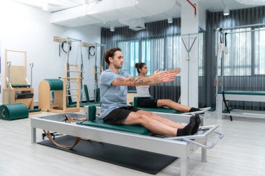 Genç bir adam ve genç bir kadın pilates egzersizleri yapıyorlar.