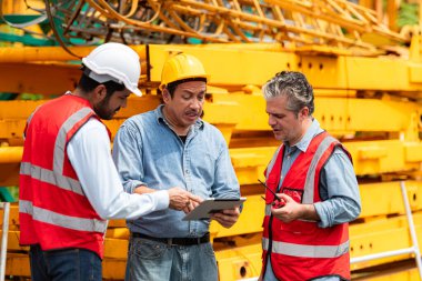 İnşaat vinç teftişinde çalışan ustabaşı ve işçiler, vinçin inşaat sahasında monte edilmesi için depodan taşınması için yapılır.