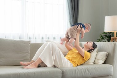 Oturma odasındaki kanepede annesiyle mutlu bir şekilde gülümseyen küçük bir çocuk.