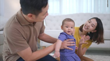 Ebeveynler ve küçük çocukları evin oturma odasında mutlu bir şekilde oynuyorlar.