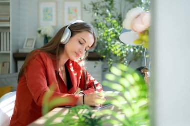 Masada otururken kulaklıklı genç bir kadın müzik dinliyor.