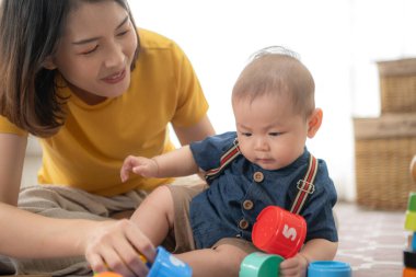 Küçük bir çocuk neşeyle oyuncaklarla oynuyor salonun zemininde annesiyle.