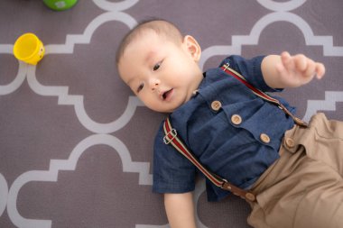 Küçük bir çocuk yerde yatar ve salonda mutlu bir şekilde gülümser.