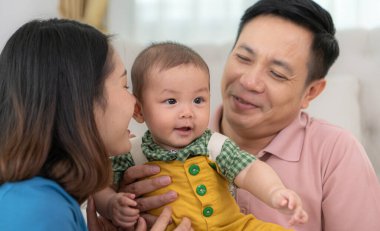 Ebeveynler ve küçük çocukları evin oturma odasında mutlu bir şekilde oynuyorlar.