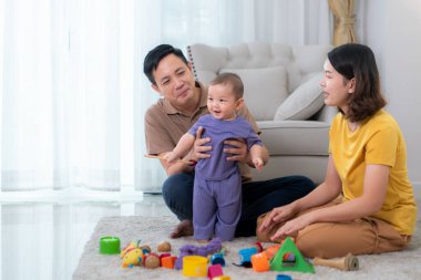 Ebeveynler ve küçük çocukları evin oturma odasında mutlu bir şekilde oynuyorlar.