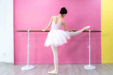 Bir kız bale öğrencisi pembe ve beyaz bir geçmişle evde bale yapıyor.