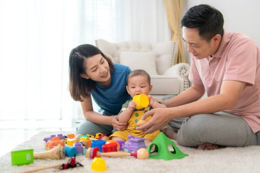 Ebeveynler ve küçük çocukları evin oturma odasında mutlu bir şekilde oynuyorlar.