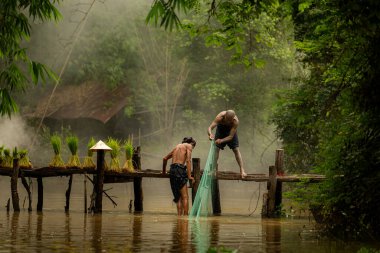 Çiftçi, nehirde balık yakalamak için balık ağı kullanan balıkçıya yardım eder ve onunla konuşur.