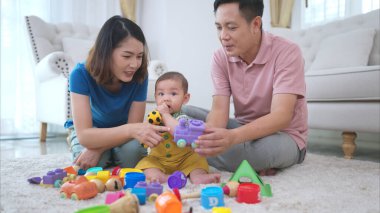 Ebeveynler ve küçük çocukları evin oturma odasında mutlu bir şekilde oynuyorlar.