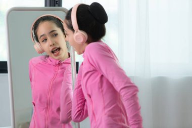 Pembe eşofmanlı bir kız bale öğrencisi en sevdiğiniz müzikle kulaklıkla dans ederek vücudu ısıtıyor.