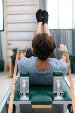 Genç bir adam pilates egzersizi yapıyor. Bir pilates reformcusu üzerinde.