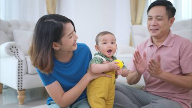 Ebeveynler ve küçük çocukları evin oturma odasında mutlu bir şekilde oynuyorlar.