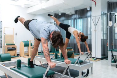 Genç bir adam ve genç bir kadın pilates egzersizleri yapıyorlar.