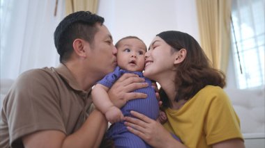 Ebeveynler ve küçük çocukları evin oturma odasında mutlu bir şekilde oynuyorlar.