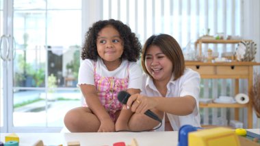 Küçük bir kız ve anne oyuncak bir masaya oturur, mikrofonu tutar ve neşeyle salonda şarkı söyler.