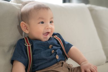 Küçük bir çocuk oturma odasındaki kanepede mutlu bir şekilde oturuyor.