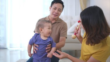 Ebeveynler ve küçük çocukları evin oturma odasında mutlu bir şekilde oynuyorlar.