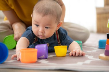 Küçük bir çocuk neşeyle oyuncaklarla oynuyor salonun zemininde annesiyle.