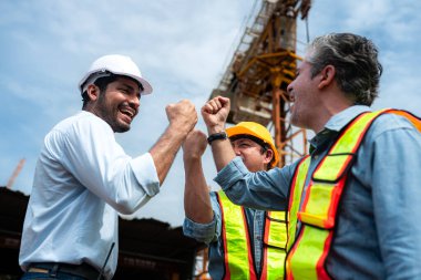 İnşaat alanında çalışan bir grup işçi, arka planda bir vinçle inşaat sürecini tartışıyorlar.