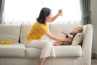 Oturma odasındaki kanepede annesiyle mutlu bir şekilde gülümseyen küçük bir çocuk.
