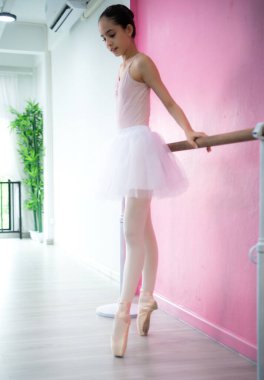 Bir kız bale öğrencisi pembe ve beyaz bir geçmişle evde bale yapıyor.