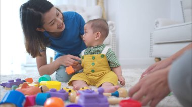 Ebeveynler ve küçük çocukları evin oturma odasında mutlu bir şekilde oynuyorlar.