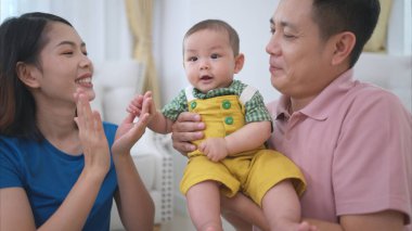 Ebeveynler ve küçük çocukları evin oturma odasında mutlu bir şekilde oynuyorlar.