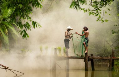 Çiftçi, nehirde balık yakalamak için balık ağı kullanan balıkçıya yardım eder ve onunla konuşur.