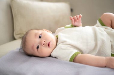 Küçük bir çocuk yatakta mutlu bir şekilde gülümsüyor ve annesi çocuk kulaklarını temizlemek için pamuk tomurcuk kullanıyor.