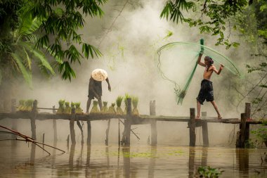 Çiftçi, nehirde balık yakalamak için balık ağı kullanan balıkçıya yardım eder ve onunla konuşur.