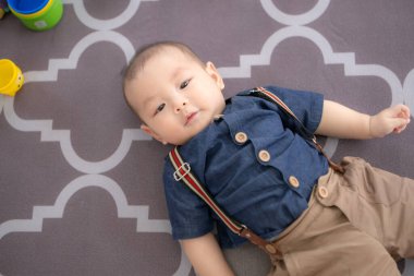 Küçük bir çocuk yerde yatar ve salonda mutlu bir şekilde gülümser.