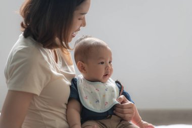Oturma odasındaki kanepede annesiyle mutlu bir şekilde gülümseyen küçük bir çocuk.