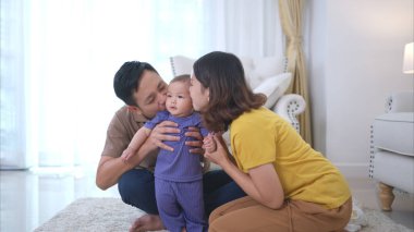 Ebeveynler ve küçük çocukları evin oturma odasında mutlu bir şekilde oynuyorlar.