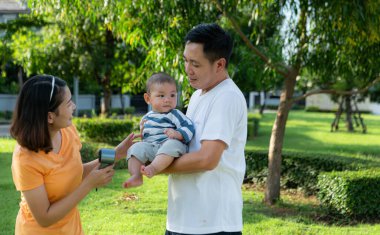 Küçük çocuklu ebeveynler parkta dinleniyor ve eğleniyorlar.