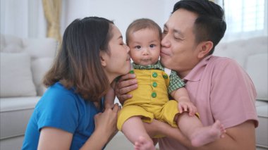 Ebeveynler ve küçük çocukları evin oturma odasında mutlu bir şekilde oynuyorlar.