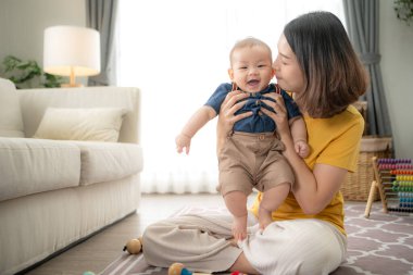 Küçük bir çocuk neşeyle oyuncaklarla oynuyor salonun zemininde annesiyle.