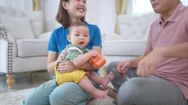 Ebeveynler ve küçük çocukları evin oturma odasında mutlu bir şekilde oynuyorlar.