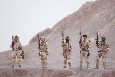 Kamuflaj üniformalı askerler silah taşıyorlar engebeli dağlarda keşif görevleri, saldırı piyade eğitimi alıyorlar..