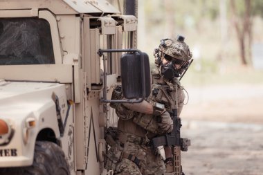 Kamuflaj üniformalı askerler, askeri haberleşme aracının yan tarafında saklanarak silahlarını ateşe hazır tutuyorlar.