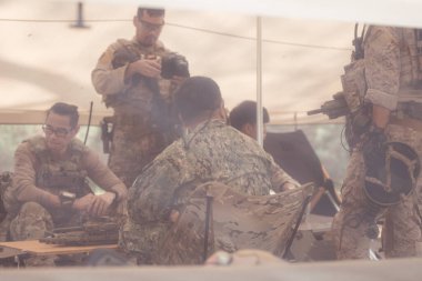 Kamuflaj üniformalı bir grup asker bir çadır kurup savaş eğitimi için hazırlanıyorlar..