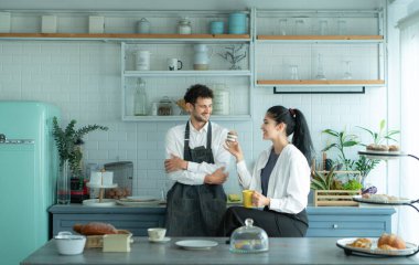Bir koca karısıyla yemek pişirirken önlük giyer. İkili kahve yudumlamak ve tamamlanmış ekmeği tatmak için mola verdi..