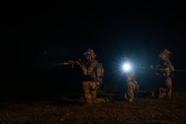 Kamuflaj üniformalı bir grup asker gece devriye görevlerinde silah taşıyor.