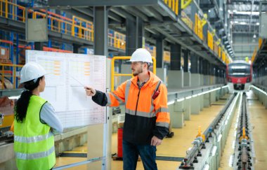 Erkek ve kadın mühendisler bir elektrik tamir istasyonunda birlikte çalışıyorlar, elektrik tren tamir programının detaylarını kontrol edin..