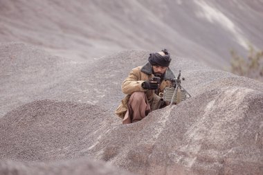 Bir Taliban askeri elinde makineli tüfekle çöl dağlarındaki savaş meydanında müttefik askerlere teslim olur.