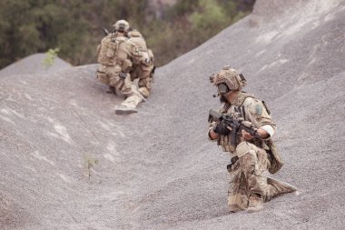Kamuflaj üniformalı askerler silah taşıyorlar engebeli dağlarda keşif görevleri, saldırı piyade eğitimi alıyorlar..