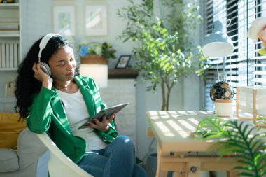 Masada otururken kulaklıklı genç bir kadın müzik dinliyor.