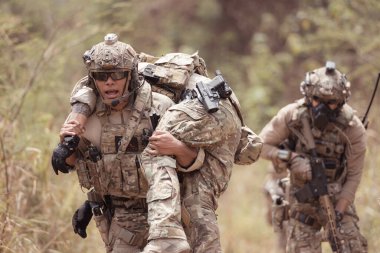 Kamuflaj üniformalı askerler silah taşıyorlar. Tropikal orman bölgesinde keşif görevleri var. Yaralıların vurulmasına yardım etmek için.