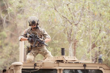 Kamuflaj üniformalı askerler bir askeri iletişim aracının çatısına ateş etmeye hazırlar.