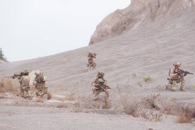 Kamuflaj üniformalı askerler silah taşıyorlar engebeli dağlarda keşif görevleri, saldırı piyade eğitimi alıyorlar..